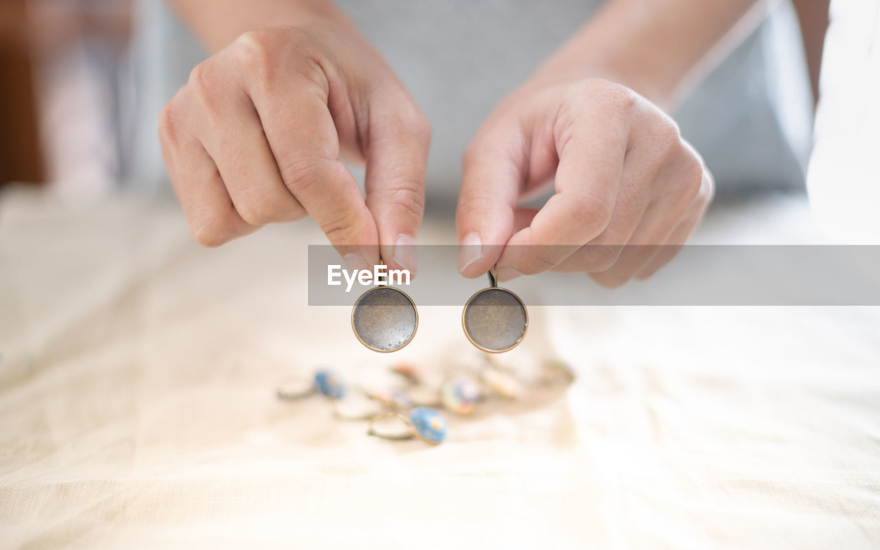 The female hands holding and choosing the wood plate frame earring for embroidery thread.