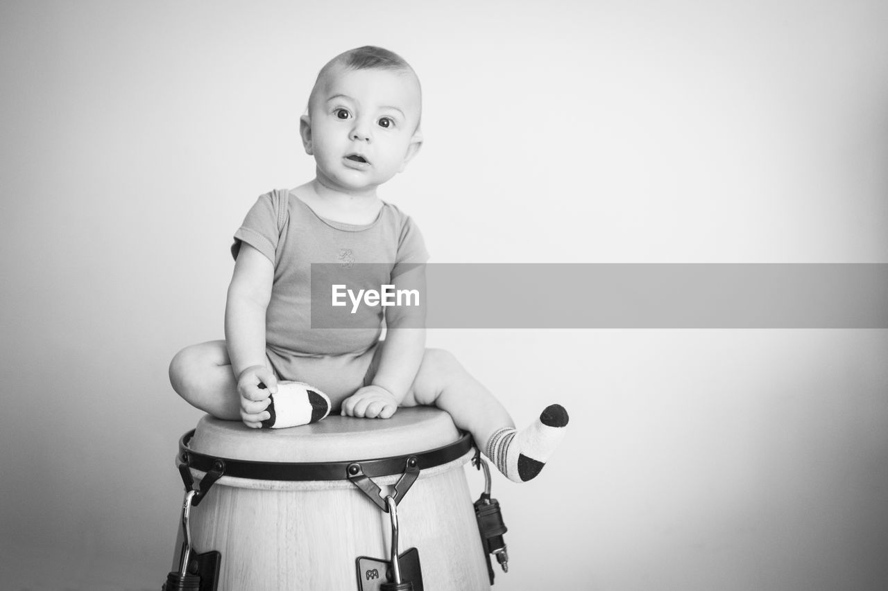 Portrait of baby boy sitting on drum against wall