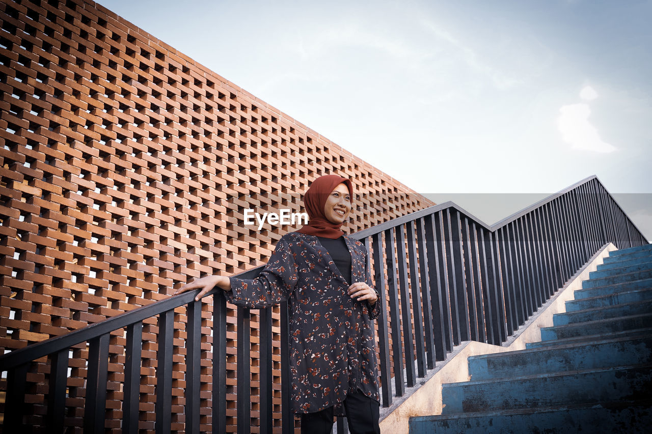 Low angle view of woman wearing hijab standing on staircase against sky