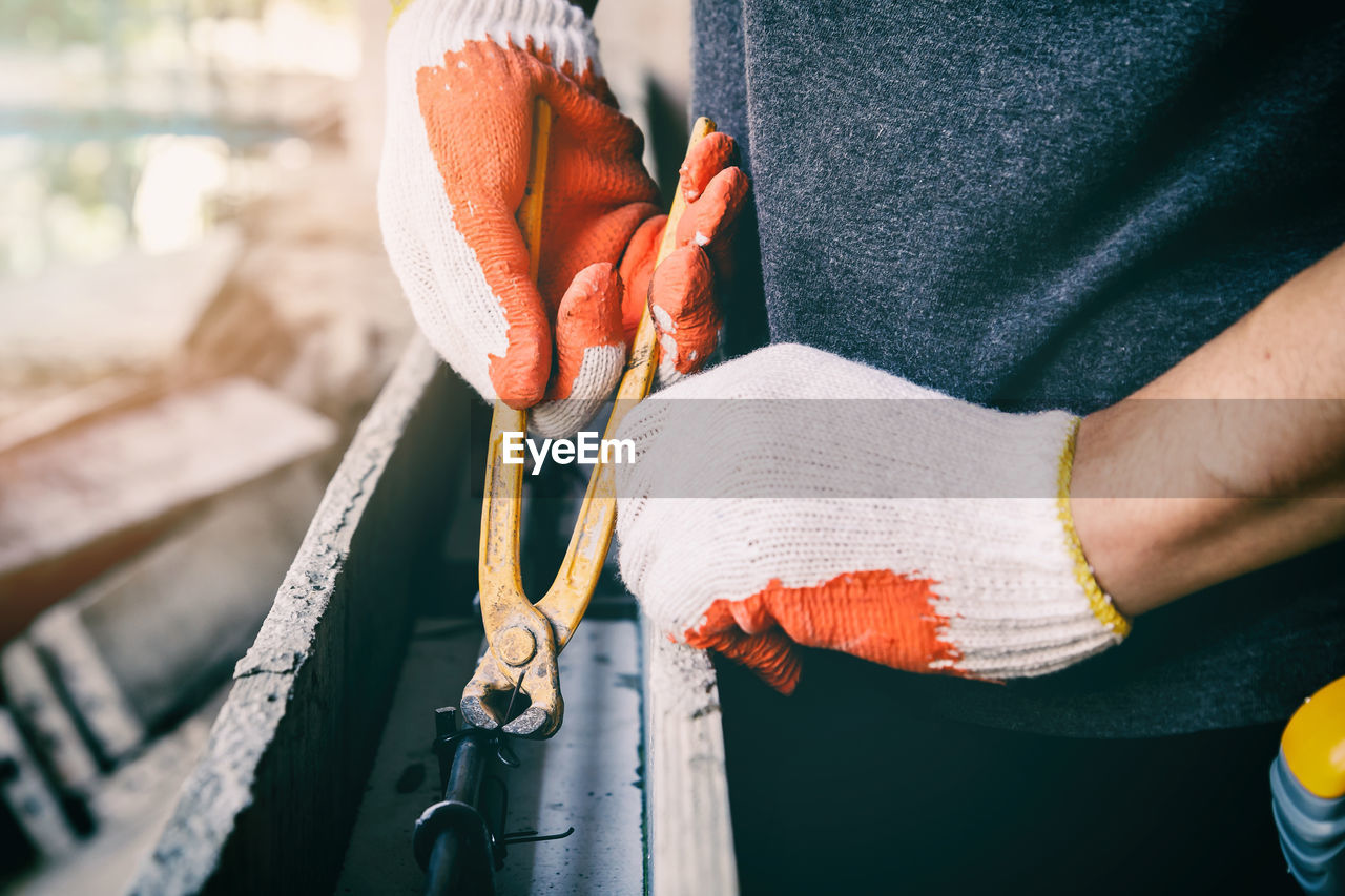 Midsection of man working on metal with pliers