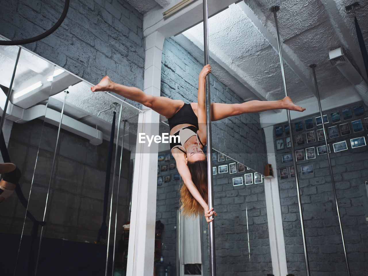 Full length of sensuous woman practicing pole dance in studio