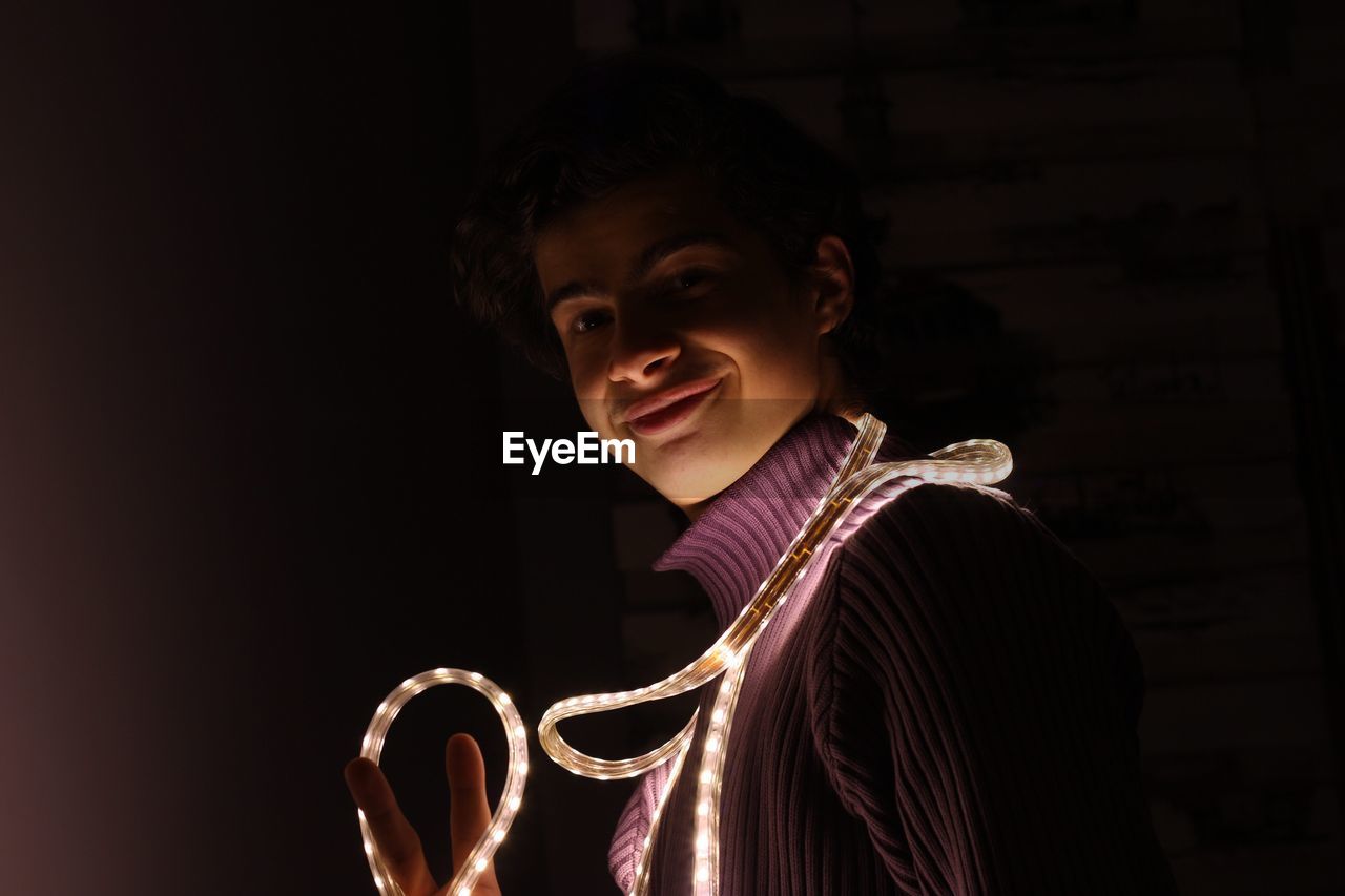 Portrait of smiling teenage boy with illuminated strip light against black background