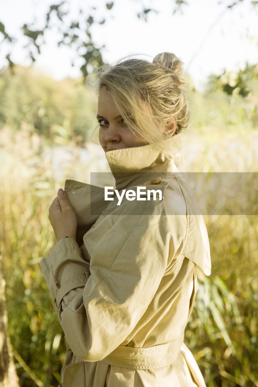 Side view portrait of young woman standing against trees