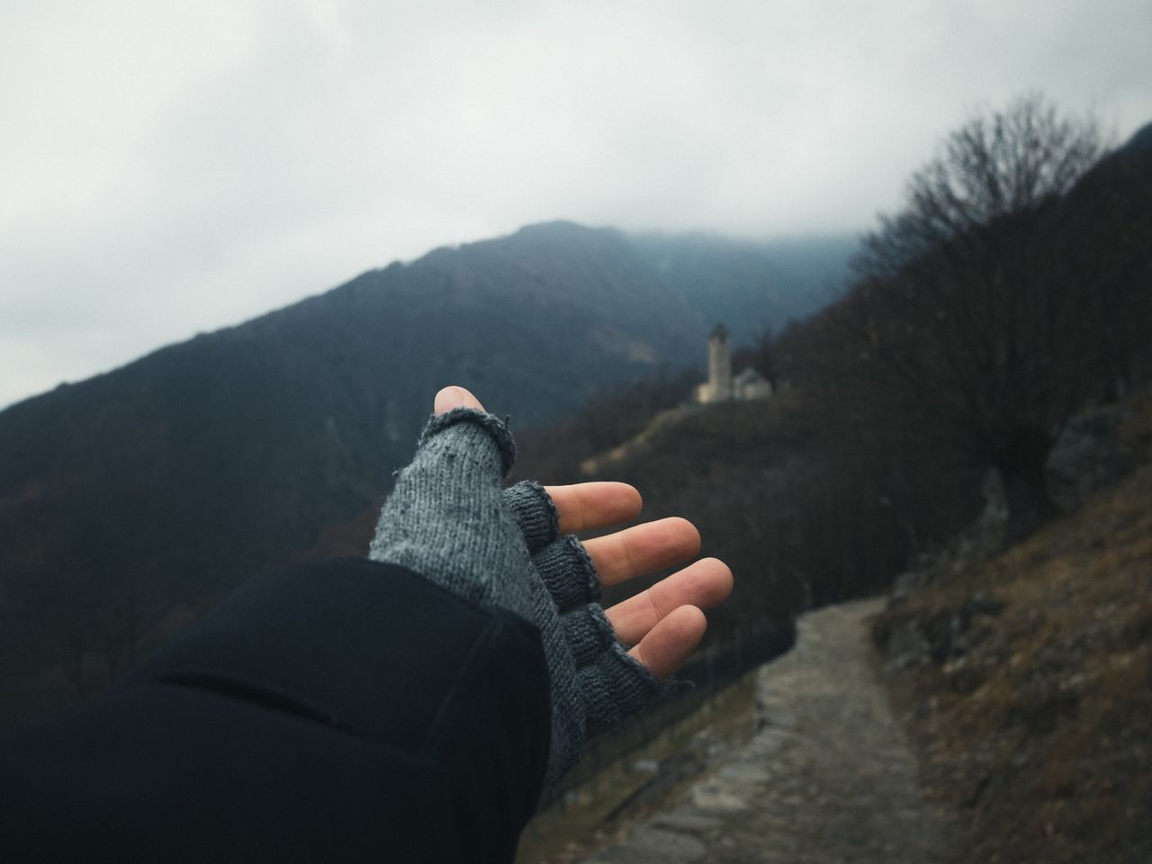 Cropped hand of person reaching mountains against sky during foggy weather