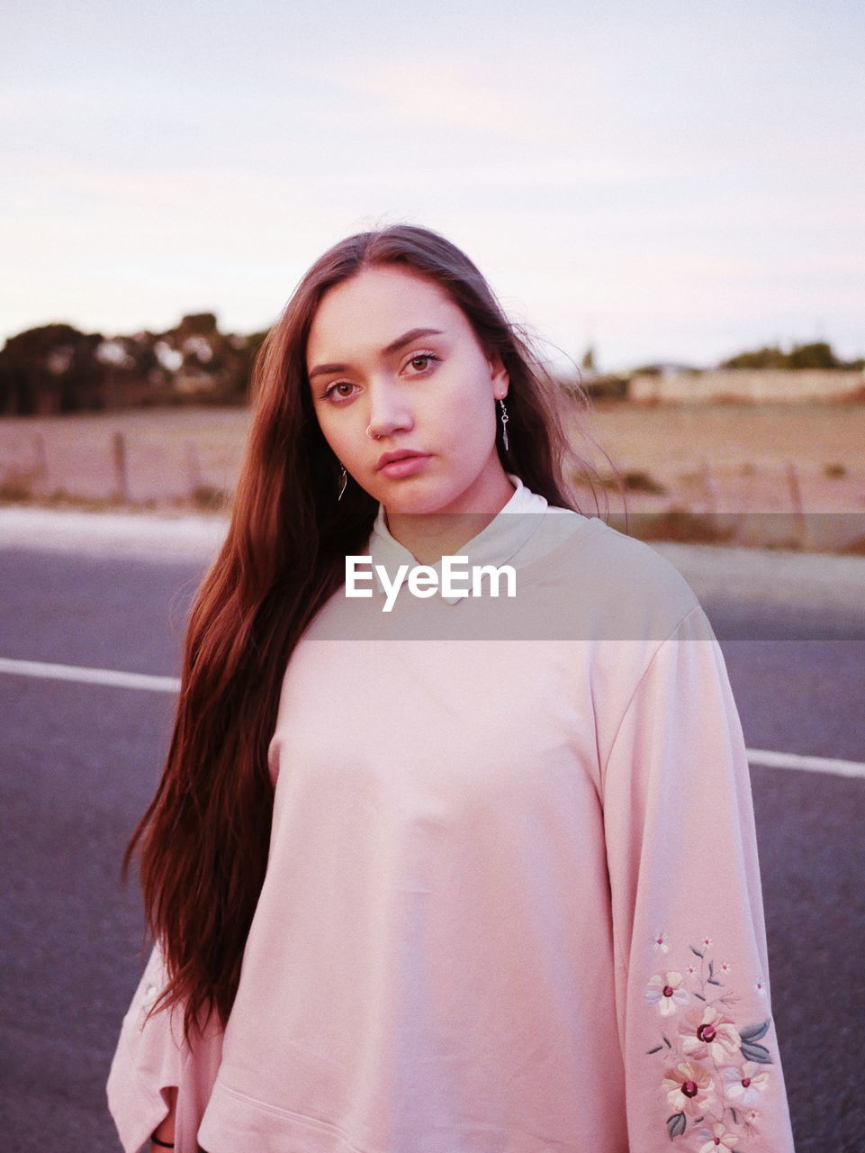 Portrait of beautiful young woman standing on road against sky