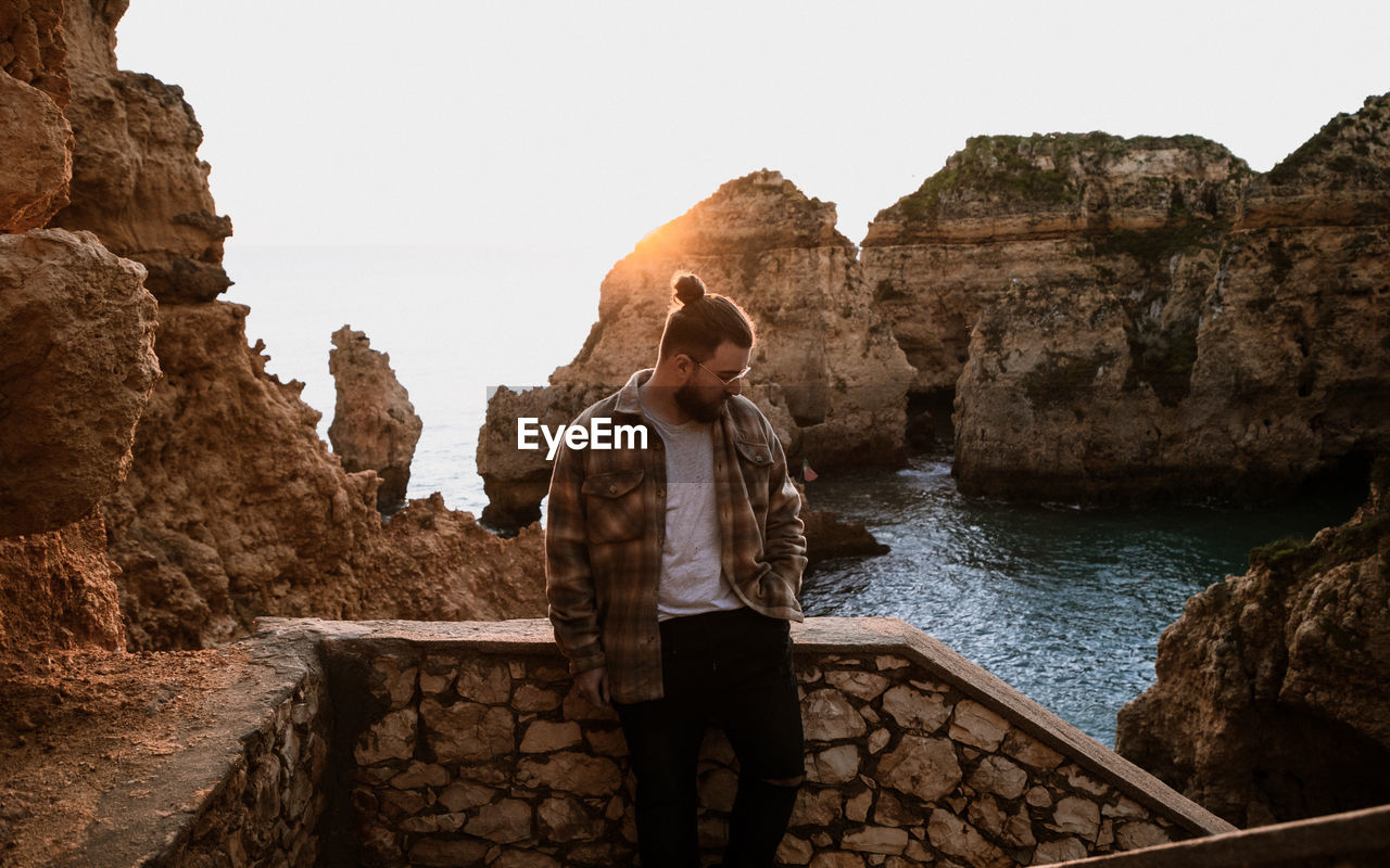Young man standing on ledge agaisnt sunrise between rock formation in sea