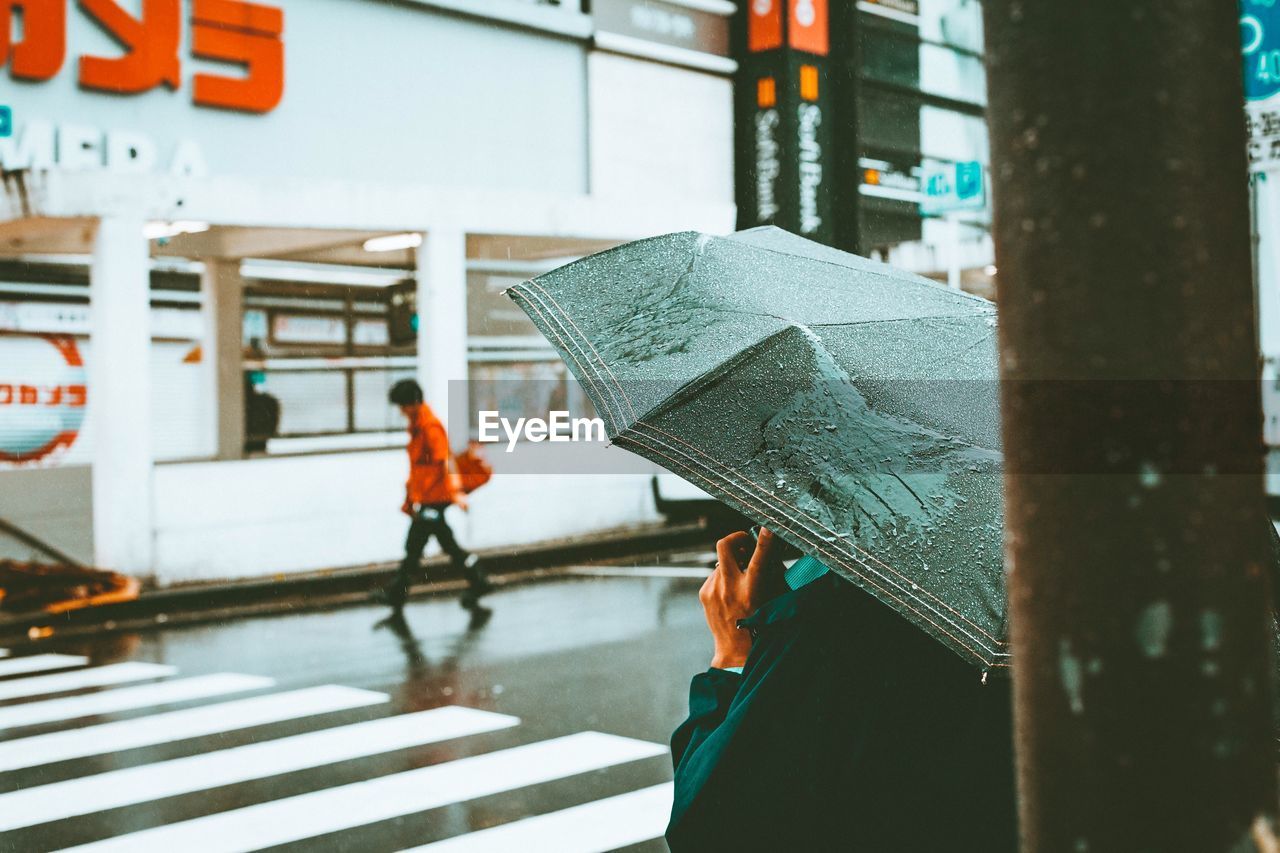 Side view of person with umbrella standing on street during rainfall
