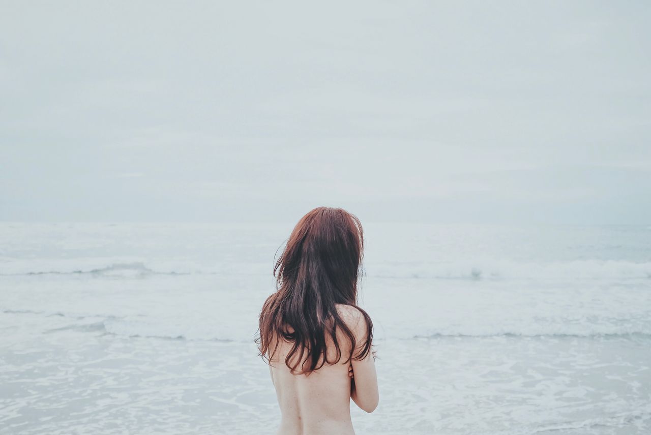 Rear view of shirtless woman standing at beach