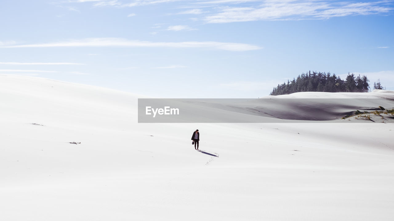 Full length of woman standing on snow against sky during sunny day