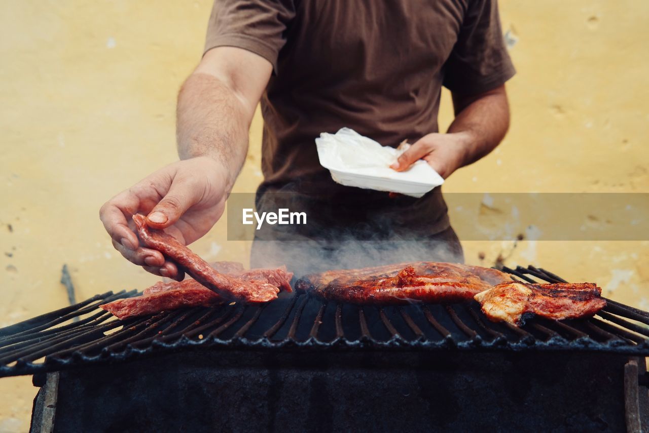 Midsection of man grilling meat against wall