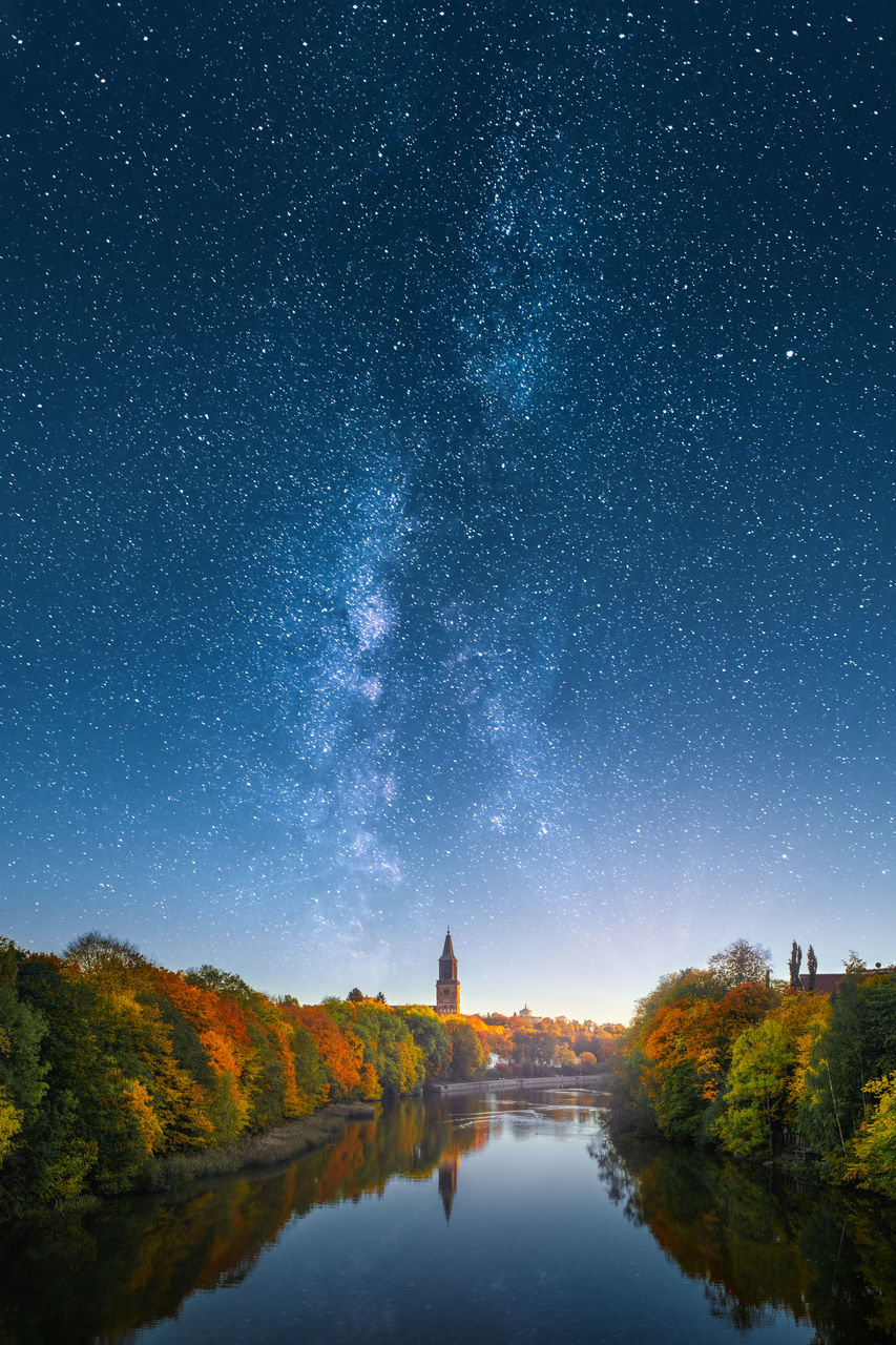 Scenic view of river amidst trees against star field in sky during autumn