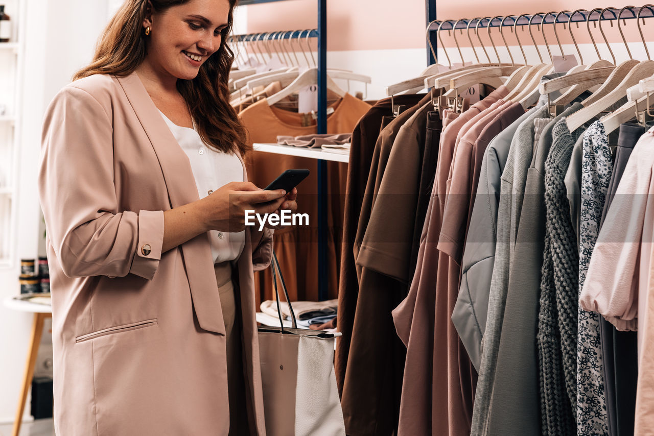 Smiling young woman using mobile phone at clothing store
