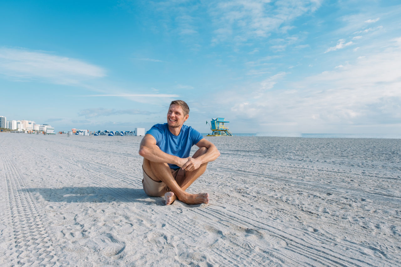 Guy walking along  miami beach. happy handsome man tourist in casual clothes sitting on sandy beach.