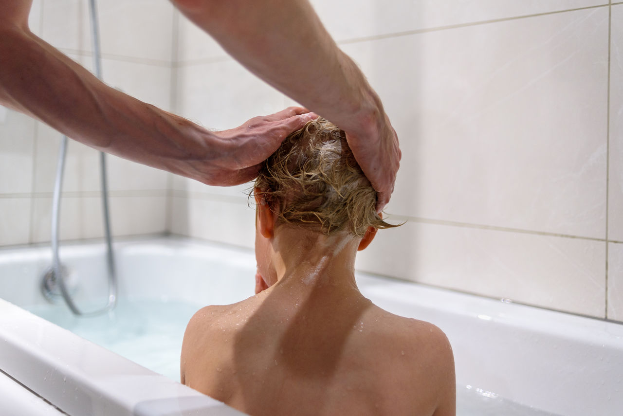 Cropped hands of person washing girls hair in bathtub