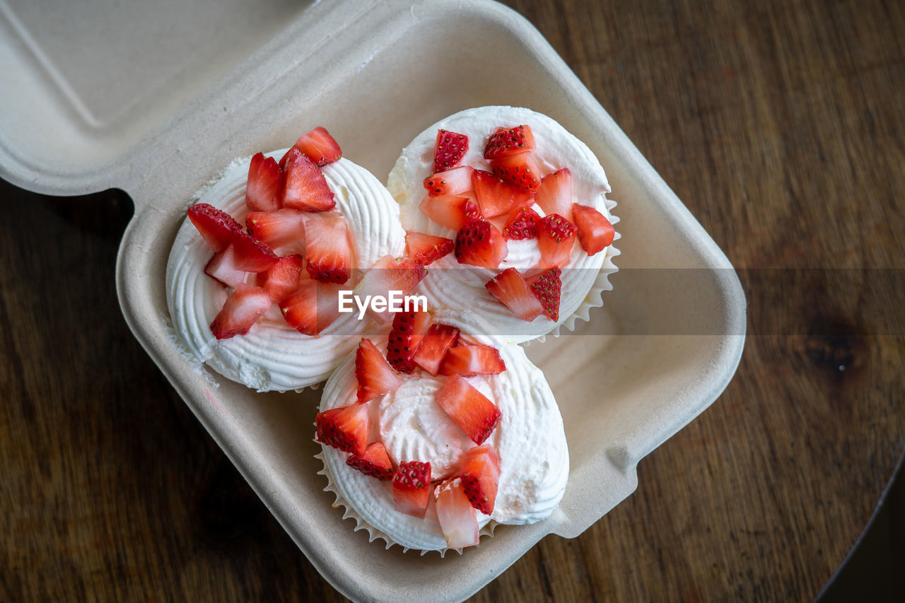 Homemade buttercream cupcakes with fresh strawberries on wooden table.