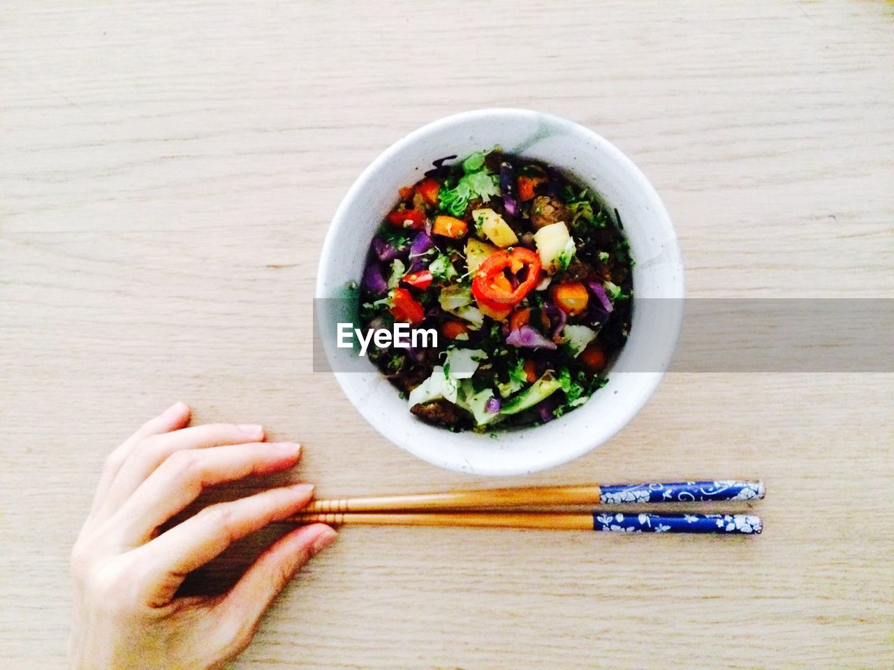 Cropped hand of woman holding chopsticks by salad bowl on table
