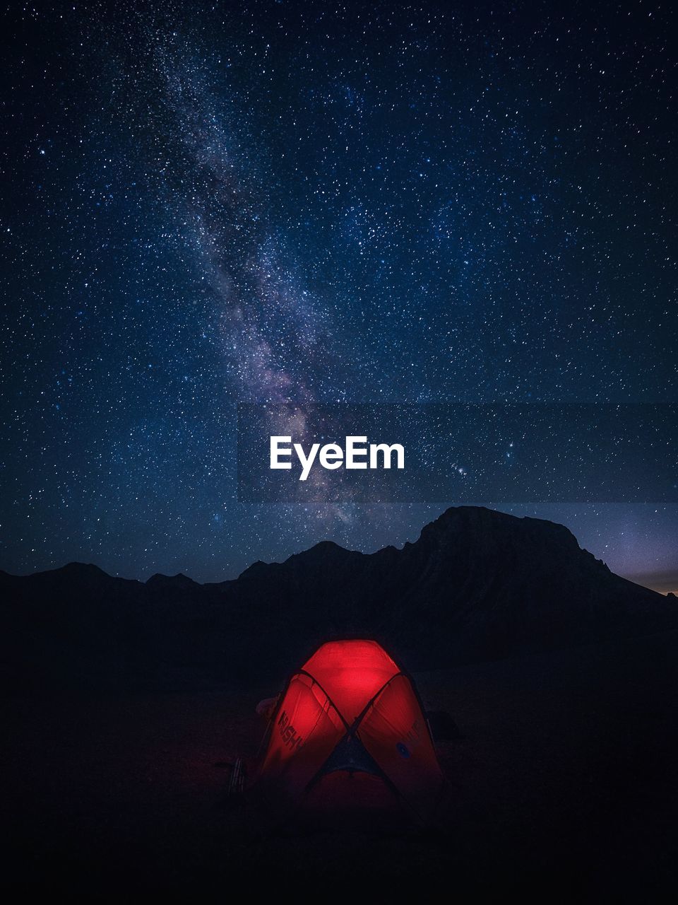 Illuminated tent on mountains against star field in sky at night