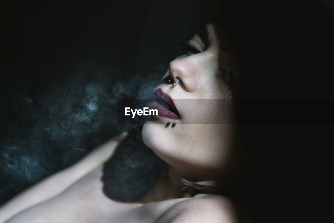 Close-up of sensual woman exhaling smoke in darkroom