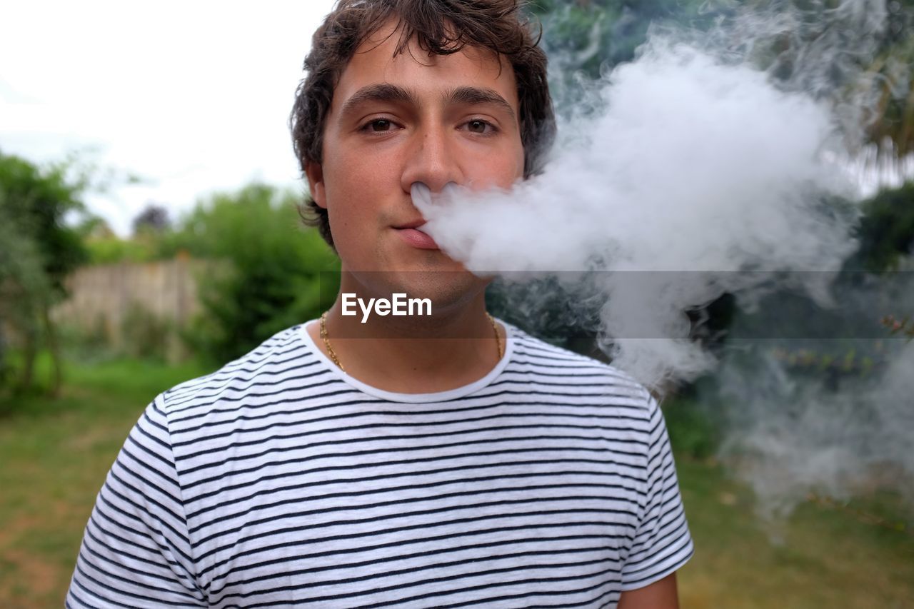Portrait of man exhaling smoke against trees