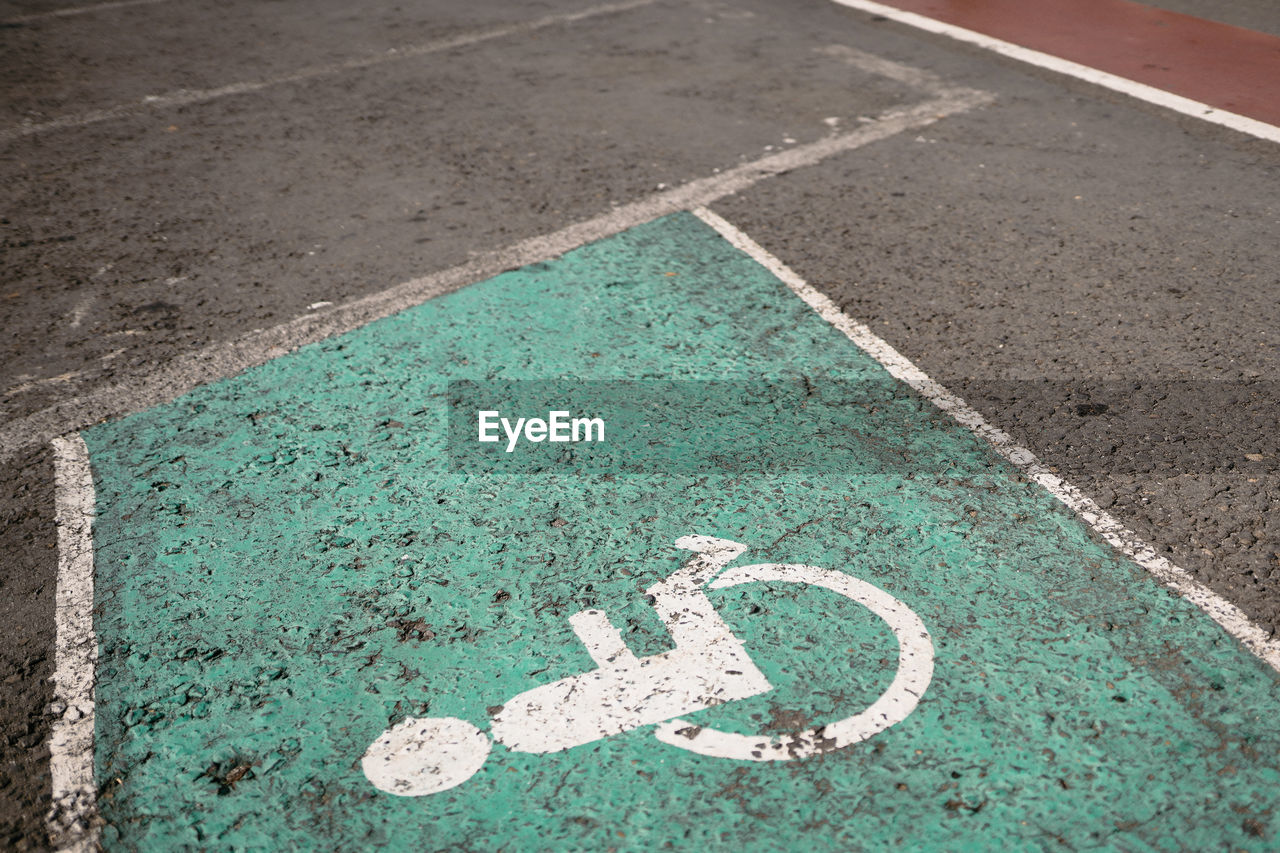 green, sign, road, high angle view, road surface, symbol, communication, no people, flooring, day, asphalt, road marking, marking, transportation, blue, city, lane, guidance, soil, street, outdoors, grass, disabled access, road sign, art, bicycle lane