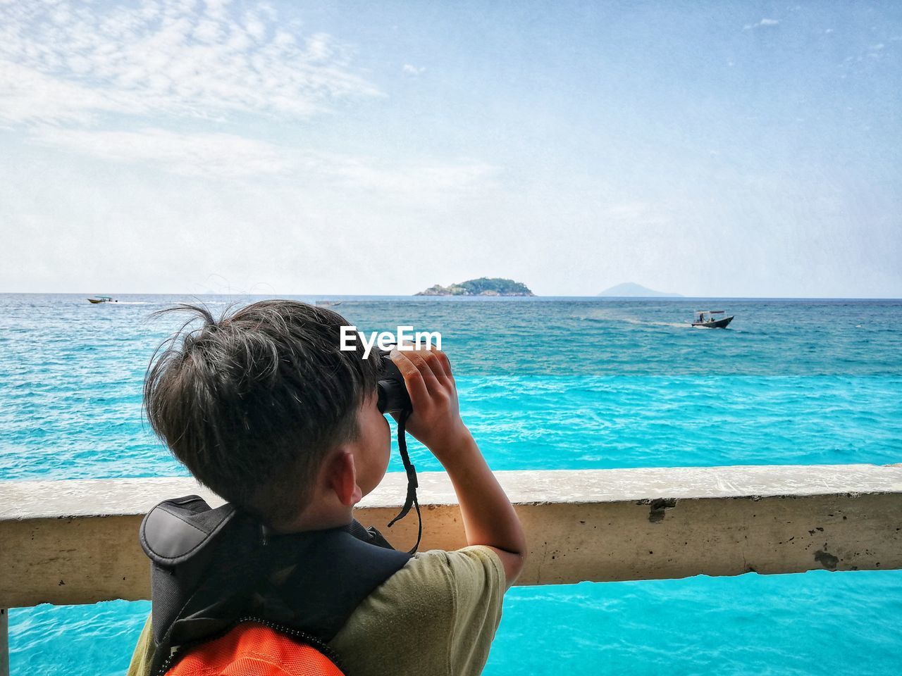 Rear view of boy looking at sea through binoculars against sky