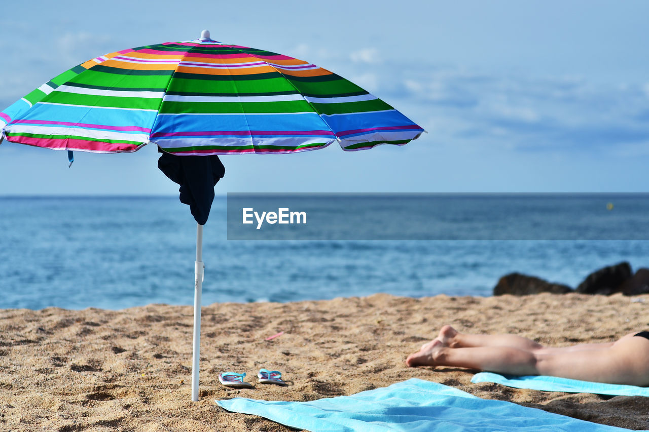Low section of women relaxing by umbrella on beach