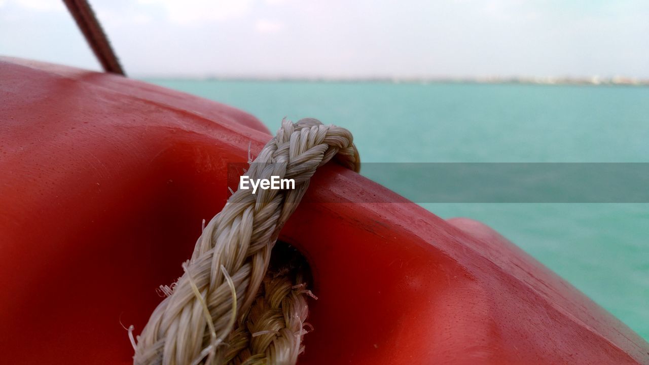 Close-up of rope tied with life belt on boat against sea and sky