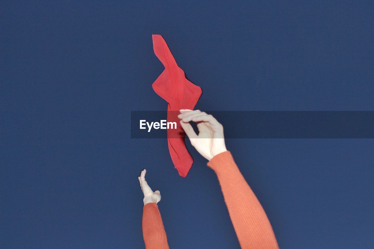 Close-up of hand holding red fabric against blue background