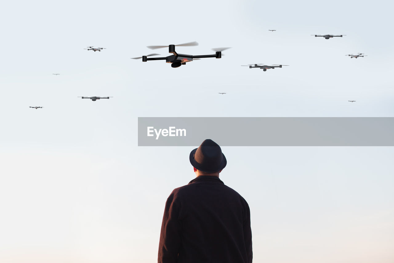 Rear view of man looking at drones flying in sky