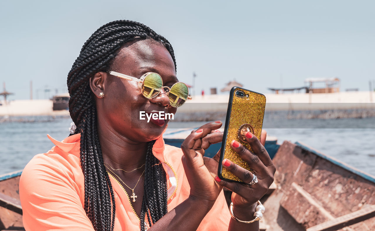 African woman sitting on a boat with mobile phone in hand and taking photos