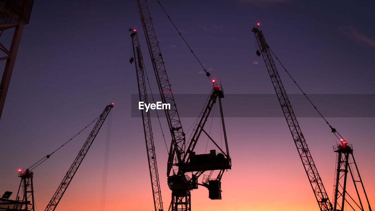 Low angle view of cranes against sky at sunset