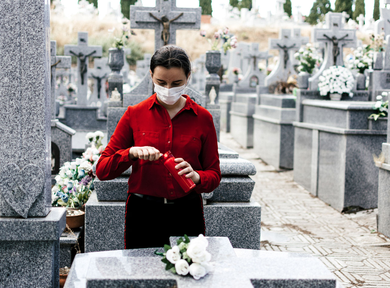 Young woman wearing mask standing at cemetery