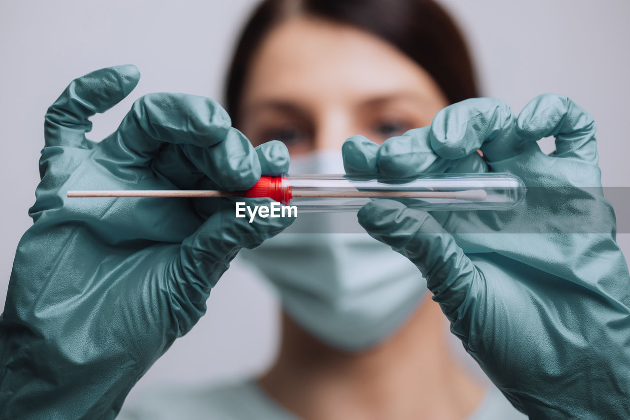 Close-up of doctor wearing mask holding test tube against gray background
