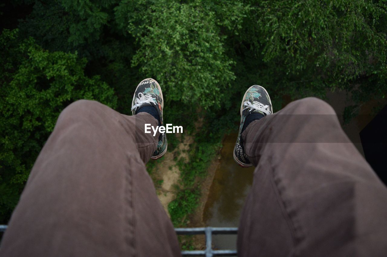 Low section of person dangling over trees by stream
