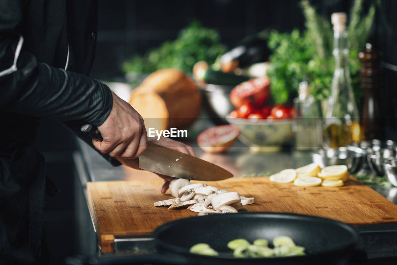 Cooking dinner - chef holding a knife, cutting mushrooms on a wooden cutting board