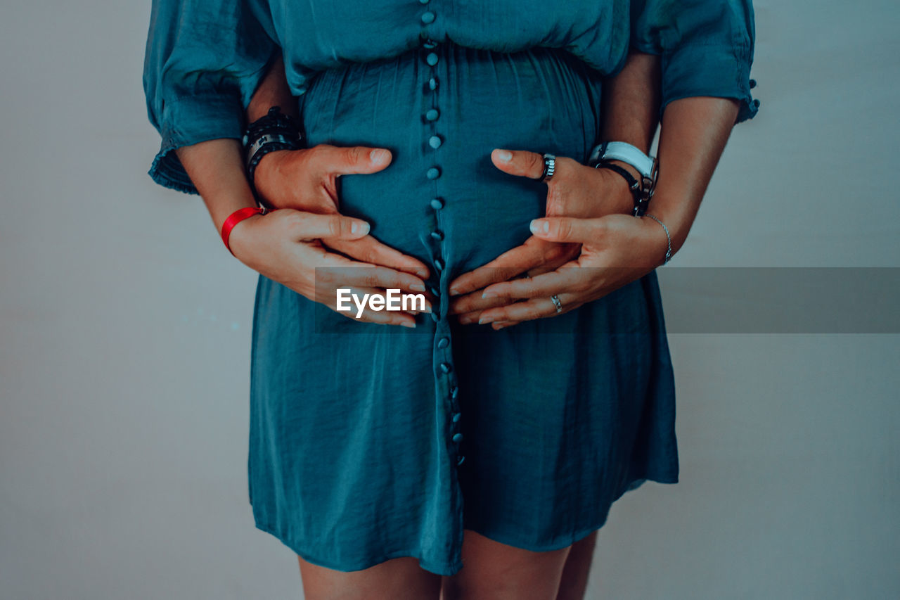 Midsection of pregnant woman with man standing against blue background