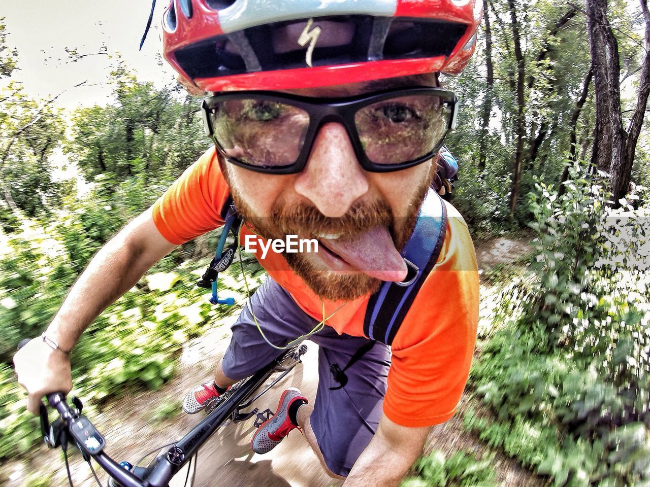 Close-up of man sticking out tongue while riding bicycle in forest