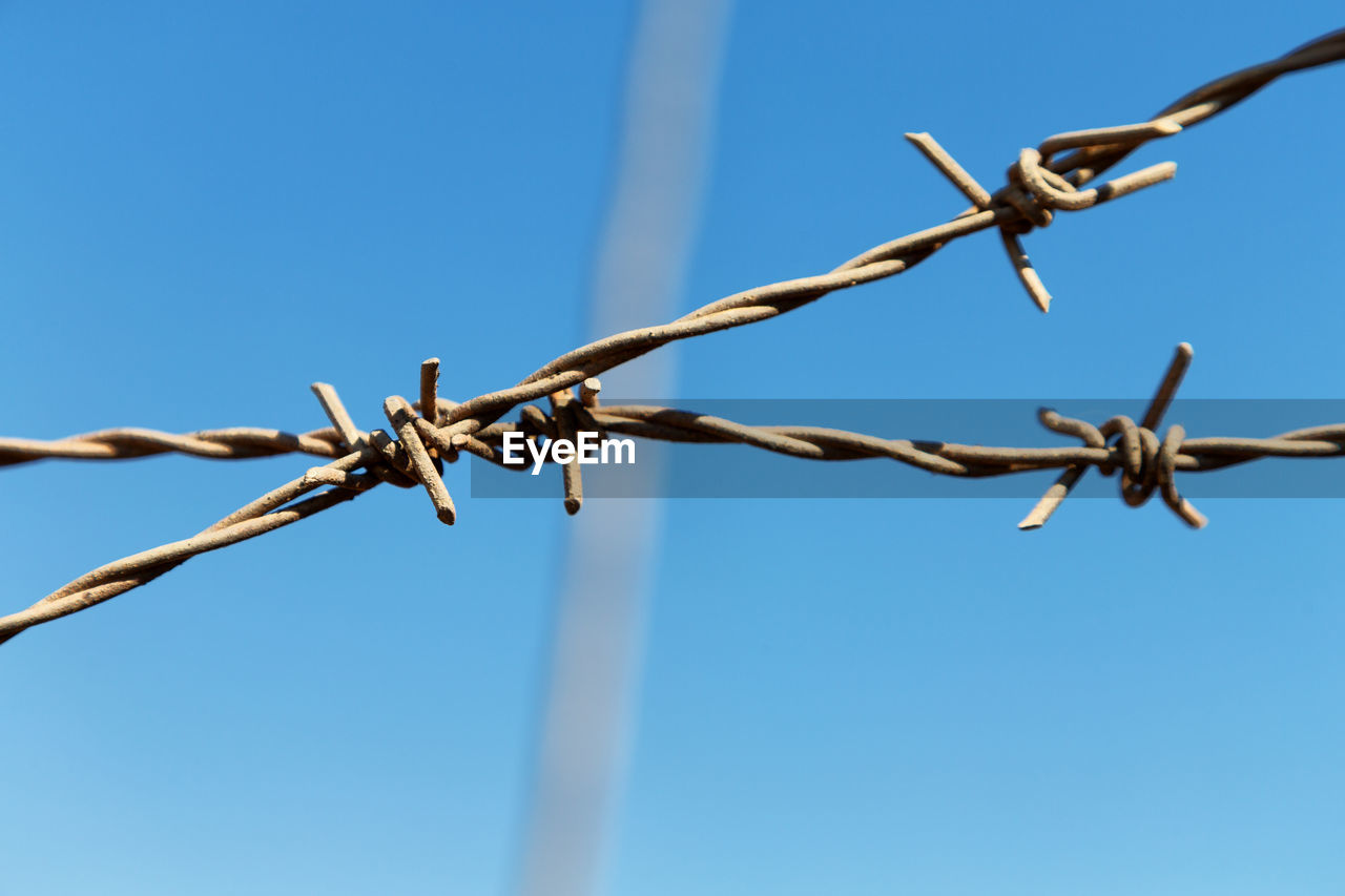 CLOSE-UP OF BARBED WIRE AGAINST CLEAR BLUE SKY