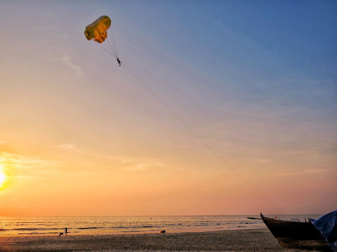 PEOPLE PARAGLIDING AT BEACH DURING SUNSET