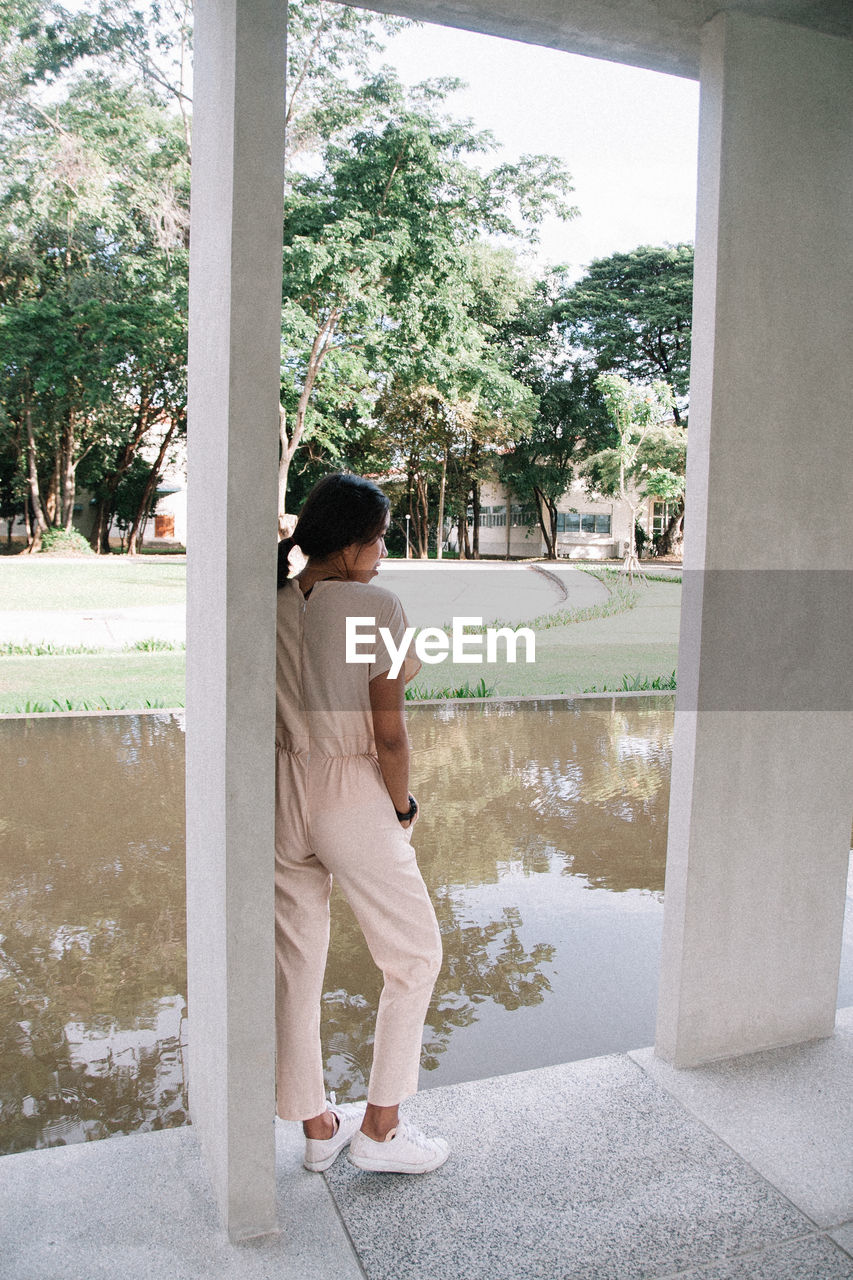 one person, full length, adult, women, plant, day, tree, nature, architecture, standing, lifestyles, clothing, window, female, water, looking, outdoors, side view, white, leisure activity, contemplation, casual clothing, footwear, relaxation, person, young adult, built structure