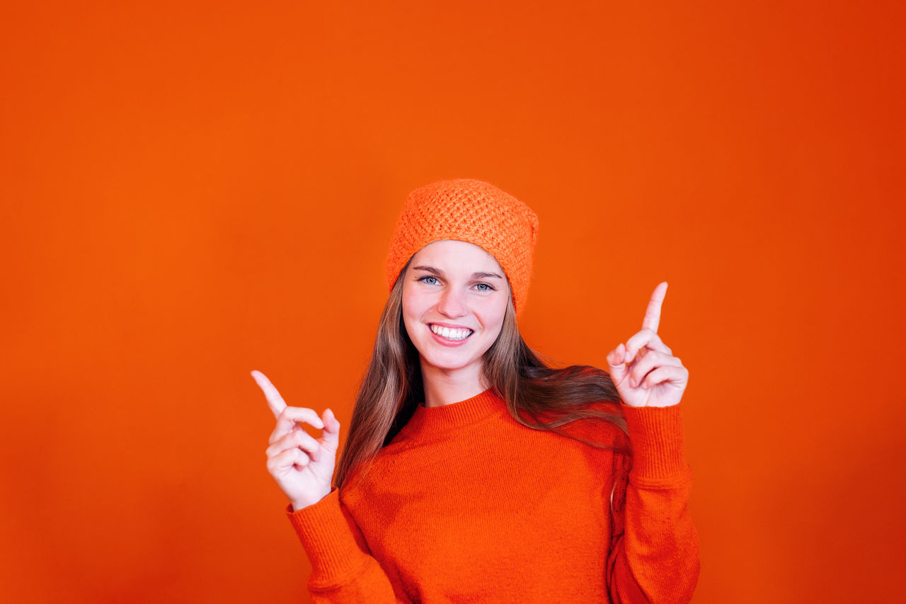 Smiling woman on vivid orange background pointing fingers up - copy space advertising