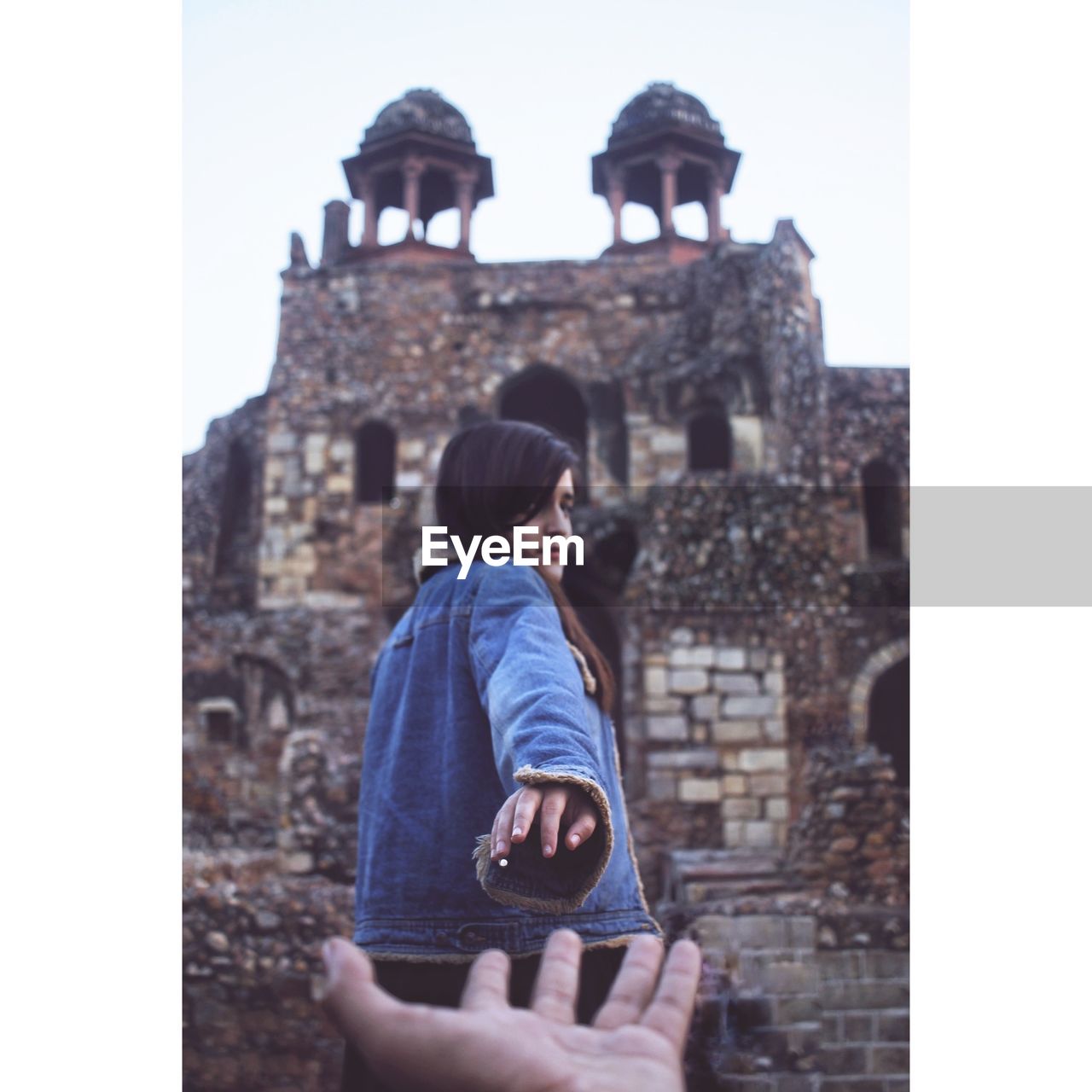 Cropped hand reaching towards woman standing against fort