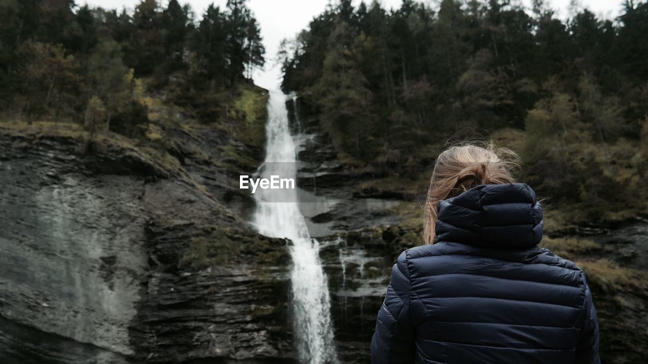Rear view of woman standing against waterfall on mountain