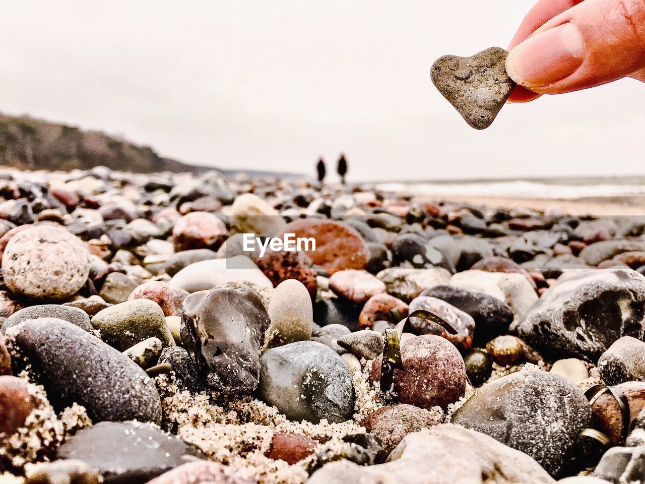 Cropped hand holding heart shaped stone at beach