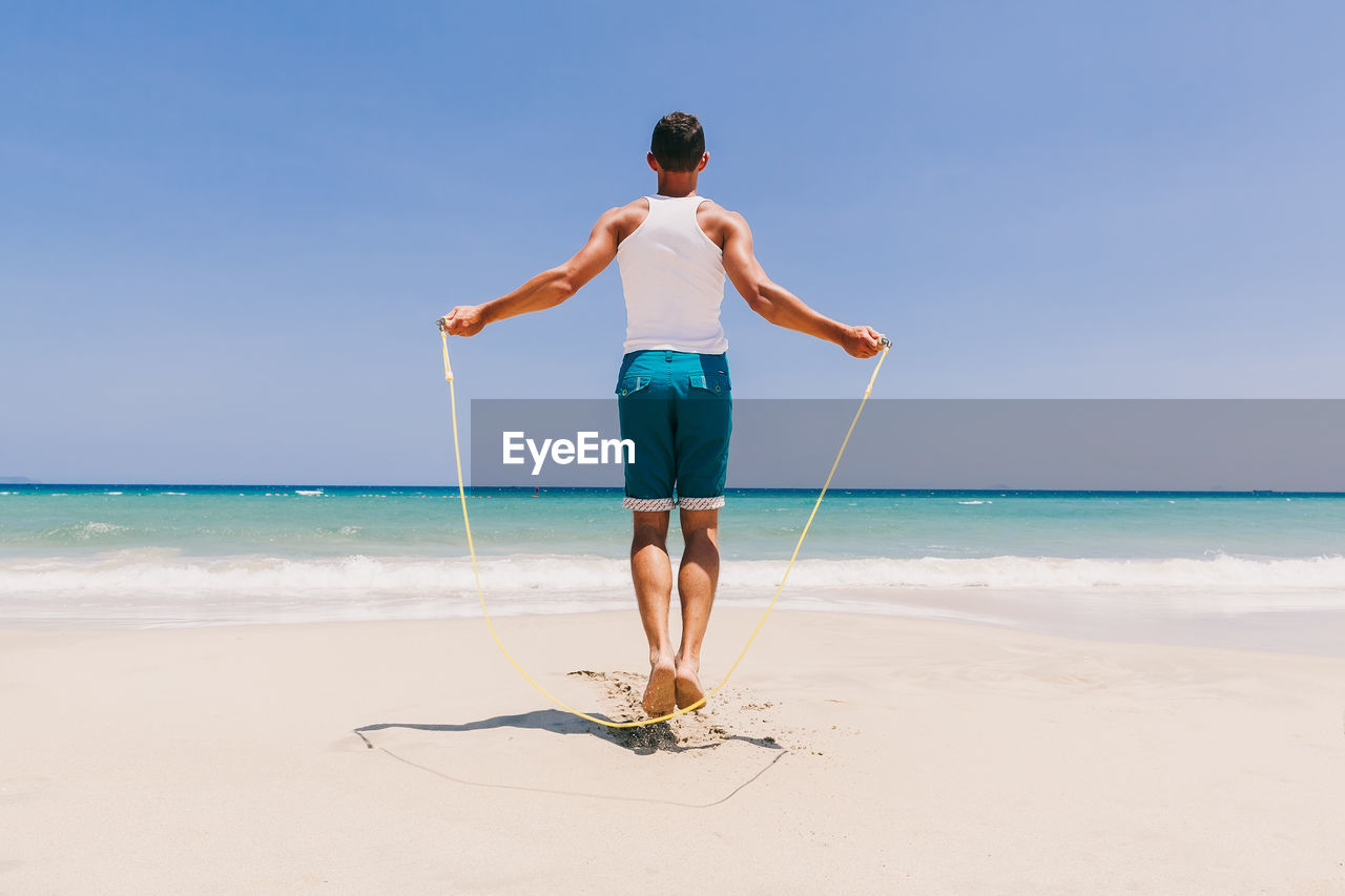 Full length of man exercising at beach against clear sky