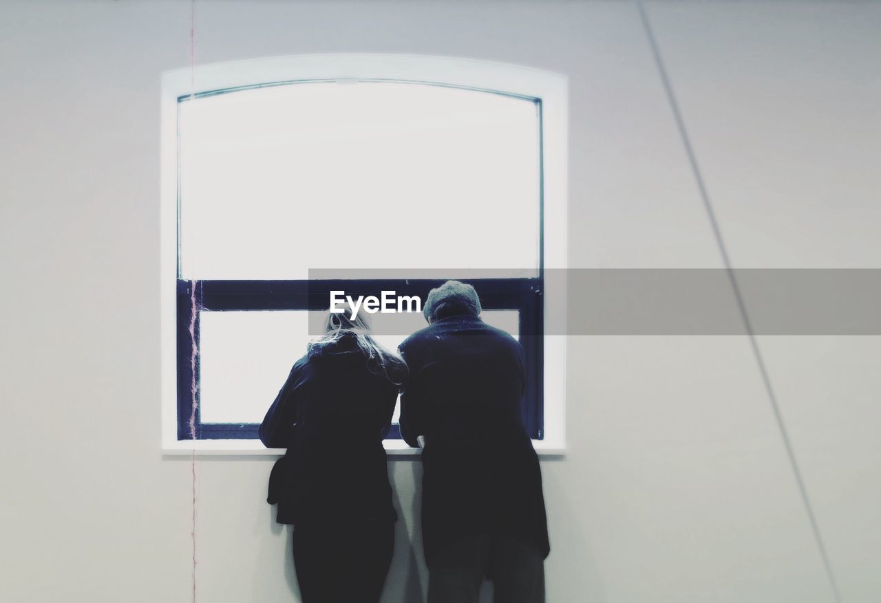 Rear view of man and woman standing at window in building
