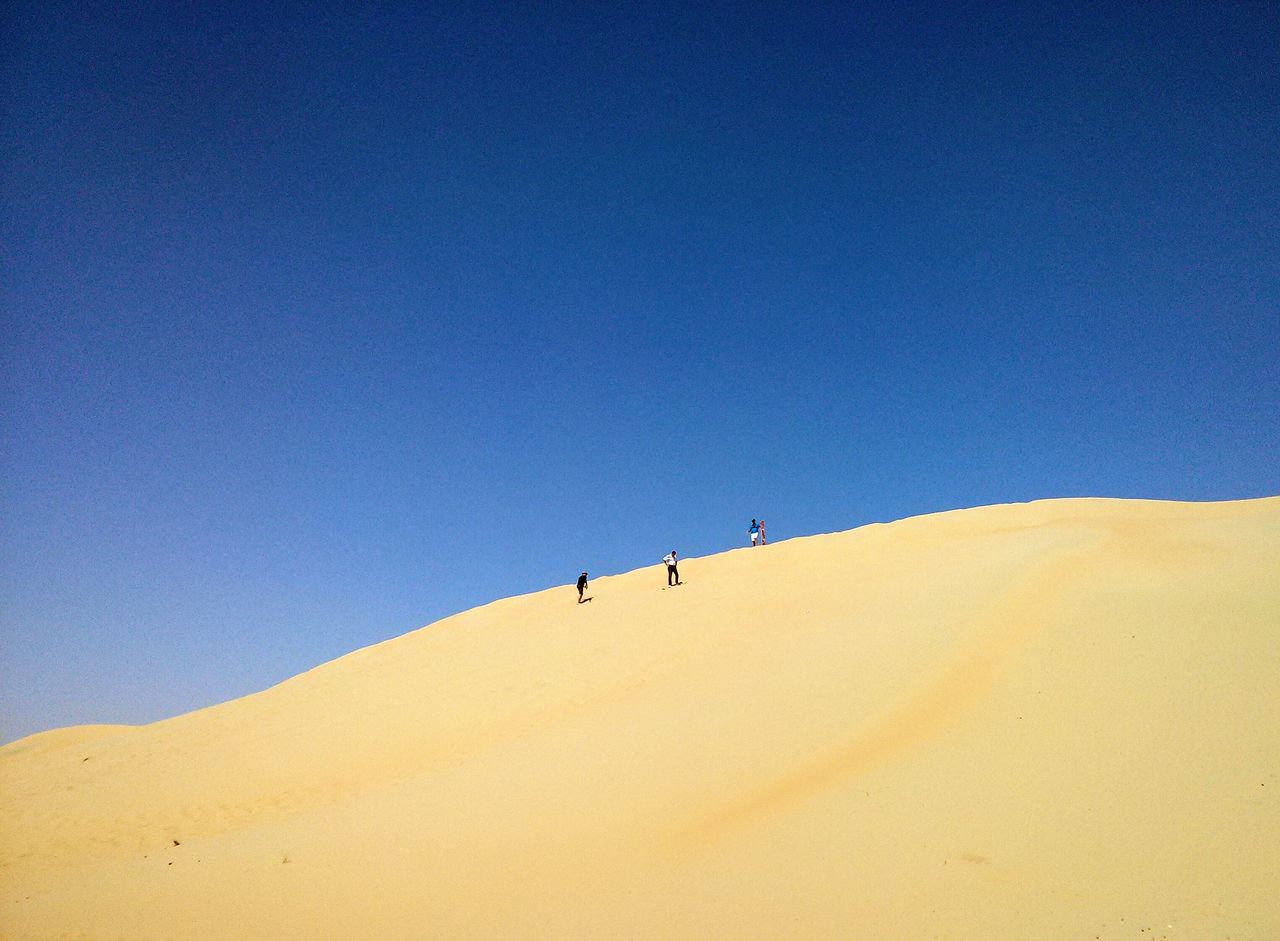 People walking in desert against clear blue sky