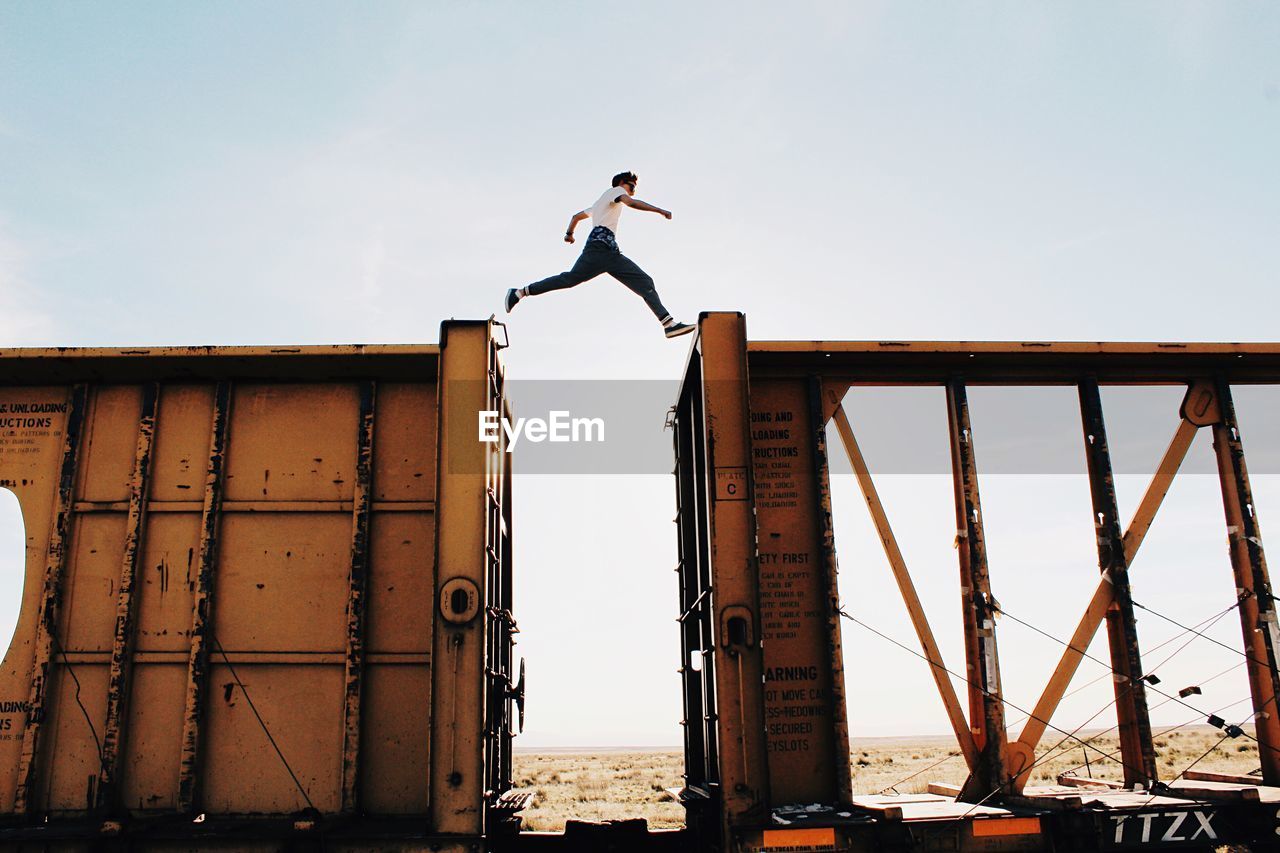 Low angle view of man jumping over metal structure against sky