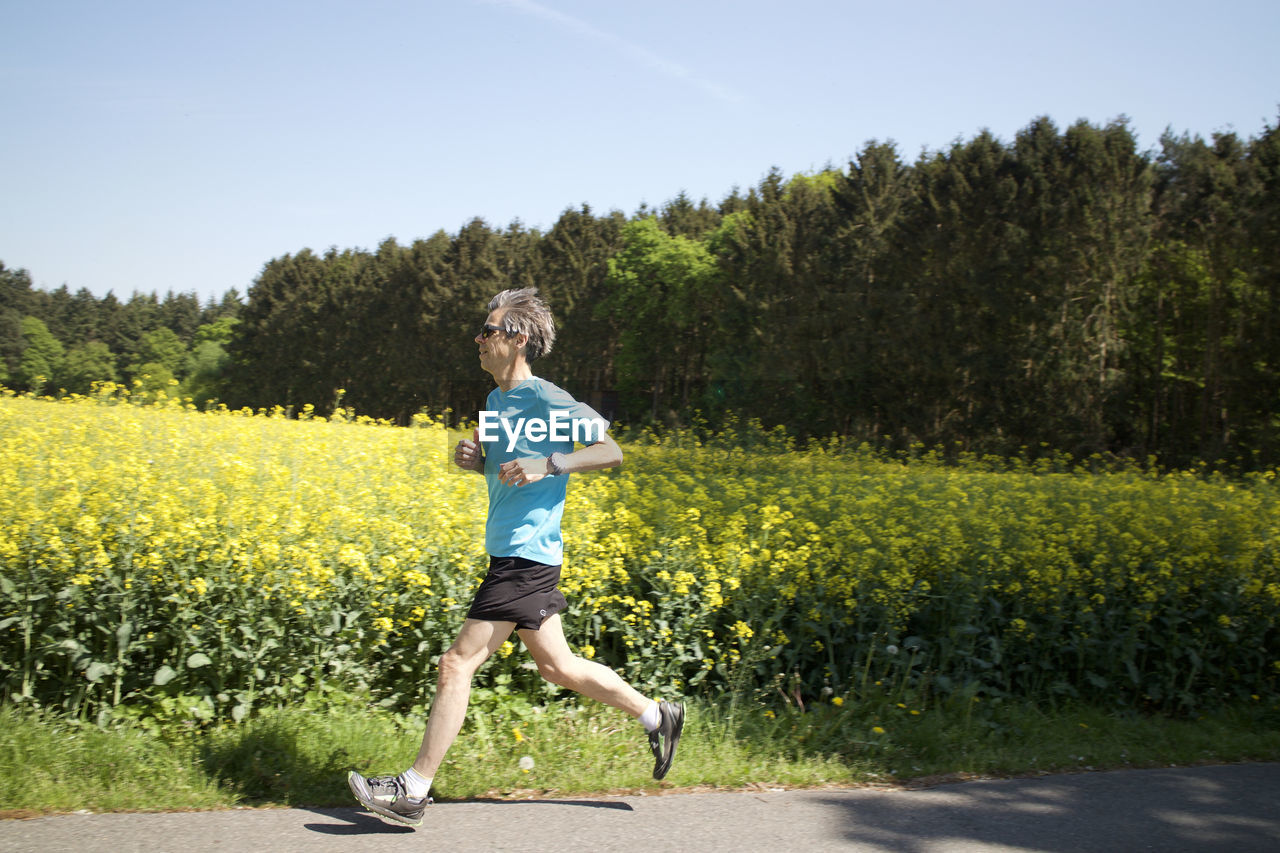 Full length side view of man running on road by yellow flowering plants