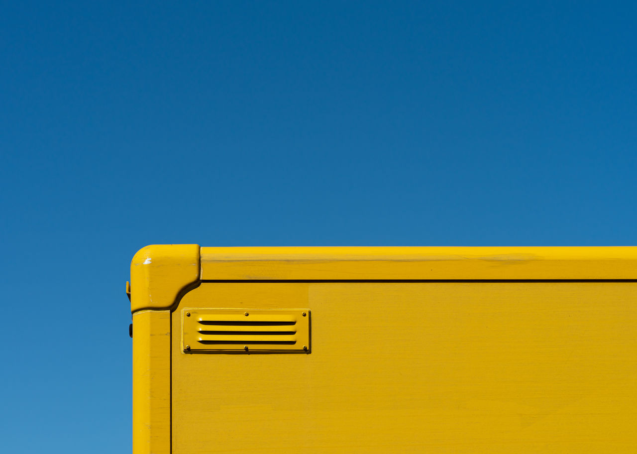 Low angle view of yellow container against clear blue sky